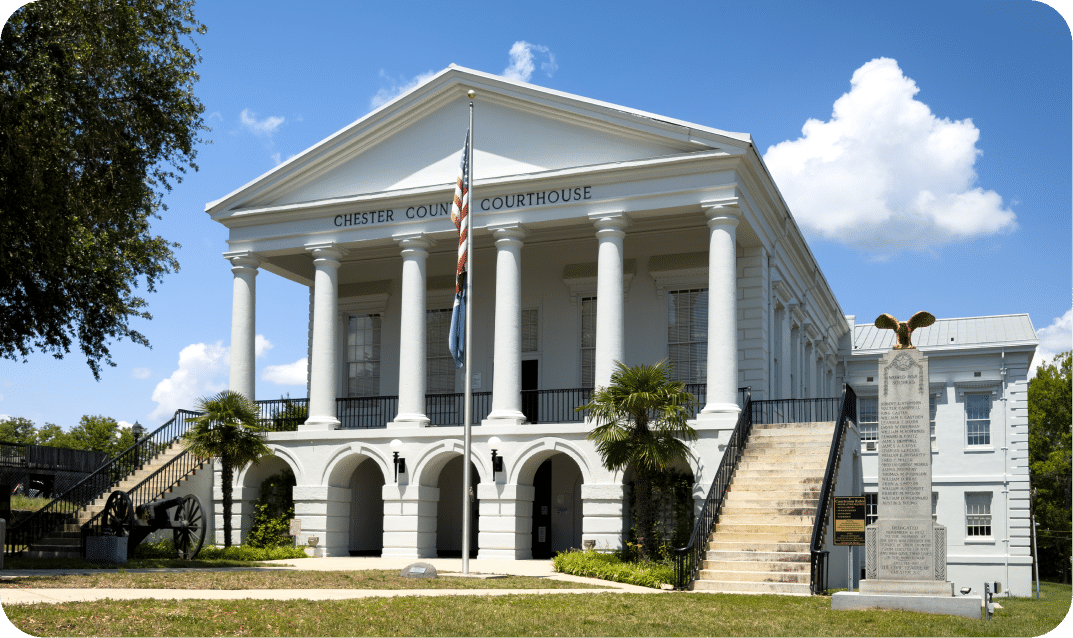 Historic Chester County Courthouse featuring a grand white-columned facade, American flag, a historic cannon, and a monument on the lawn.