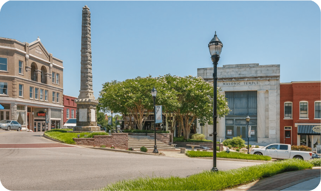 Downtown Chester town square view highlighting the historic stone obelisk monument, shade trees, and the Masonic Temple building under a clear blue sky.